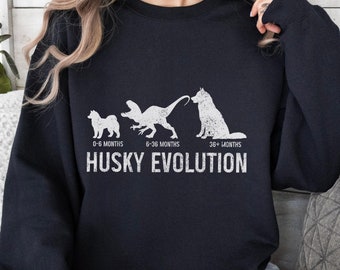 May include: Black sweatshirt with a white graphic of a husky dog evolution. The graphic shows a husky puppy, a husky growing into a dinosaur, and a full-grown husky. The text "Husky Evolution" is below the graphic.