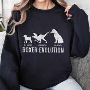 May include: Black sweatshirt with a white graphic of a boxer dog at different ages. The graphic shows the dog as a puppy, a young dog, and an adult dog. The text "BOXER EVOLUTION" is below the graphic.