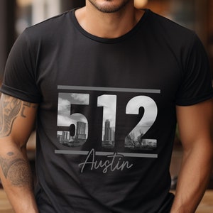 May include: Black t-shirt with a graphic design featuring the number 512 with a cityscape image inside the numbers and the word "Austin" below.