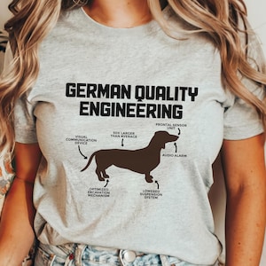 May include: A gray t-shirt with a brown dachshund silhouette and the text "German Quality Engineering". The dachshund is labeled with humorous anatomical features, such as "Visual Communication Device", "50% Larger Than Average", "Optimized Excavation Mechanism", "Lowered Suspension System", "Frontal Sensor Unit", and "Audio Alarm".