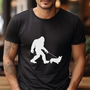 May include: Black t-shirt with a white silhouette of Bigfoot walking a corgi dog.