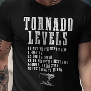 May include: Black t-shirt with the text "TORNADO LEVELS" in white, listing different tornado intensities. The shirt also features a small graphic of a tornado. A casual, everyday wear tee.