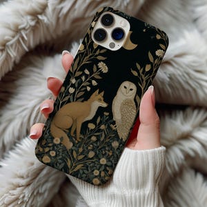May include: A black phone case featuring a fox and owl design. The case has a dark background with floral and foliage accents in gold and cream colors. A crescent moon and stars are also visible.