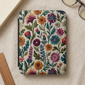 May include: A rectangular e-reader case featuring a dense, colorful botanical pattern on a cream background. The design includes various flowers in shades of yellow, orange, magenta, purple, and teal, interspersed with green leaves and stems.