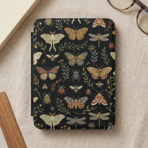 May include: A rectangular e-reader case featuring a black background with a repeating pattern of various insects including butterflies, moths, dragonflies, beetles, and bees, interspersed with small green sprigs and floral elements.