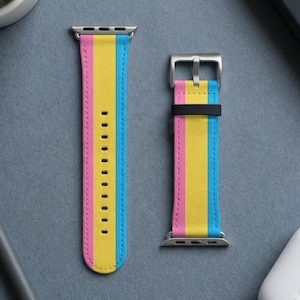 May include: A two-piece watch strap featuring a vertical striped pattern in pink, yellow, and blue. The strap includes silver-toned metal connectors and a silver-toned buckle with a black loop. The material has a smooth texture with visible stitching.