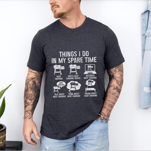 May include: Dark gray t-shirt with the text "THINGS I DO IN MY SPARE TIME" and illustrations of grilling and meat smoking activities. The shirt features a crew neck and short sleeves.