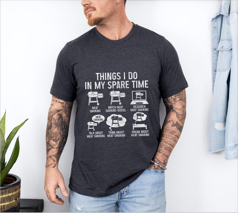 May include: Dark gray t-shirt with the text "THINGS I DO IN MY SPARE TIME" and illustrations of grilling and meat smoking activities. The shirt features a crew neck and short sleeves.