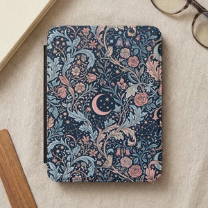Op de afbeelding: Een marineblauwe e-reader hoes met een bloemenpatroon met rozen, bladeren en een halve maan. Het ontwerp bevat roze, lichtblauwe en witte accenten. De hoes heeft een zwarte rug en een getextureerde uitstraling.