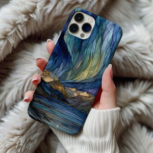 May include: A smartphone case with a stained-glass effect depicting a night scene with a lake, mountains, and a starry sky. The case has a blue, gold, and yellow colour scheme.