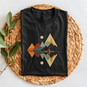 May include: Black t-shirt with a geometric design of mountains and a person kayaking on a lake. The design is in shades of blue, green, orange, yellow, and red.