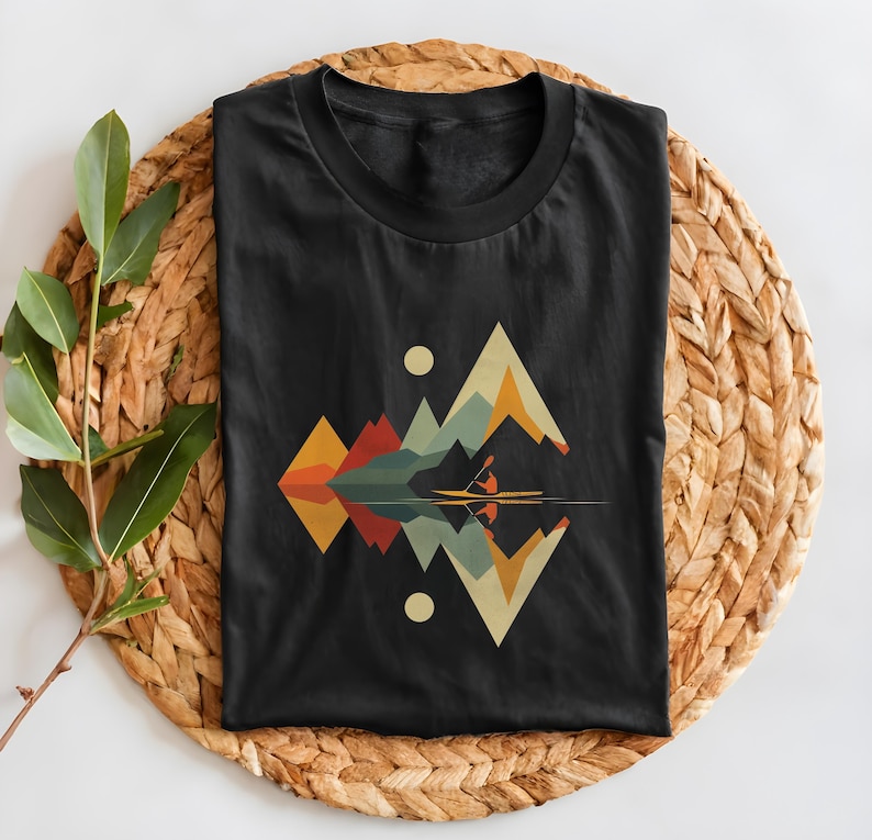 May include: Black t-shirt with a geometric design of mountains and a person kayaking on a lake. The design is in shades of blue, green, orange, yellow, and red.