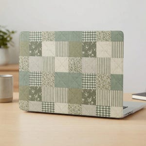 Puede incluir: Una pegatina para portátil con un patrón de colcha de retazos en verde salvia y crema. El diseño consiste en cuadrados alternos de estampados florales, rayas verticales finas, cuadros vichy pequeños y tela verde salvia sólida, unidos por costuras diagonales.
