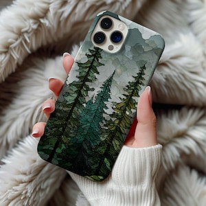 May include: A smartphone case featuring a forest scene with tall green trees and a cloudy sky. The case has a glossy finish and is held in a person's hand, showcasing the design's details. The case is designed to fit a smartphone.