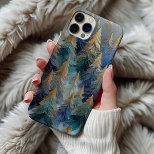 May include: A smartphone case featuring a nature-inspired design. The case showcases a pattern of stylized gold and teal-colored leaves against a blue and gray background. The case is held in a person's hand, with a soft, textured background.