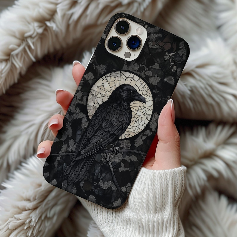 May include: Black phone case featuring a detailed illustration of a raven perched on a branch, set against a backdrop of a mosaic moon. The case has a dark, gothic aesthetic with a floral pattern.