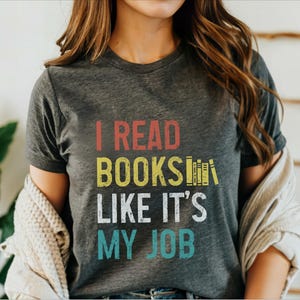 May include: A grey t-shirt with the text "I read books like it's my job" in a vintage style font. The text is in red, yellow, white, and blue.