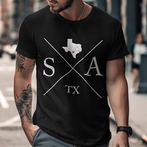 May include: A black short-sleeved t-shirt featuring a white graphic design. The design includes a map of Texas with a small red heart, the letters S and A separated by crossed white lines, and the letters TX centered below the intersection.