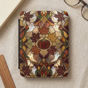 May include: A rectangular e-reader case featuring a stained glass style pattern with a central orange pumpkin, surrounded by various autumn maple leaves in shades of red, brown, and gold, interspersed with multiple small white ghost figures.