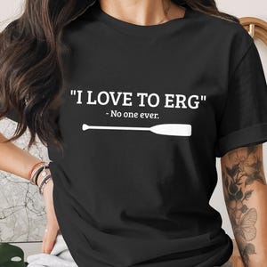 May include: Black t-shirt with the white text "I LOVE TO ERG" and "- No one ever." A white illustration of an oar is below the text. The shirt is a crew neck style.