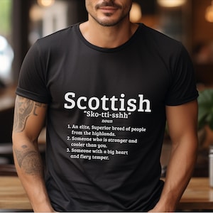 May include: A black t-shirt with white text that reads "Scottish" and "Sko-tti-sshh" with a definition of the word. The definition includes the text "An elite, Superior breed of people from the highlands."