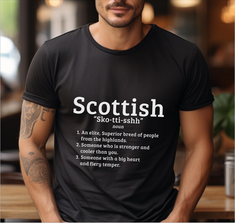 May include: A black t-shirt with white text that reads "Scottish" and "Sko-tti-sshh" with a definition of the word. The definition includes the text "An elite, Superior breed of people from the highlands."