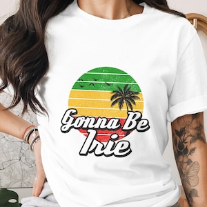 May include: White t-shirt with a colorful graphic. The graphic features a green, yellow, and red sunset design with a palm tree silhouette and the text "Gonna Be Irie" in a stylized font. The shirt is a casual wear item.