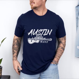 May include: A navy blue t-shirt with a white graphic of the Austin, Texas skyline with a guitar silhouette. The text "Austin Texas" is printed below the graphic.