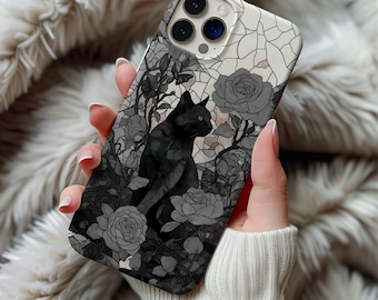 May include: A phone case featuring a black cat surrounded by gray roses and foliage. The design has a stained glass effect with a white and gray background. The case is held by a person wearing a white sweater.