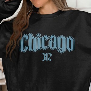 May include: Black sweatshirt with the word "Chicago" in light blue, stylized lettering. Below the word "Chicago" is the number "312" in the same light blue color. The sweatshirt is a crew neck style.