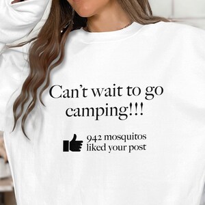 May include: White sweatshirt with the text "Can't wait to go camping!!!" in black. Below the text is a thumbs-up icon and the words "942 mosquitos liked your post".
