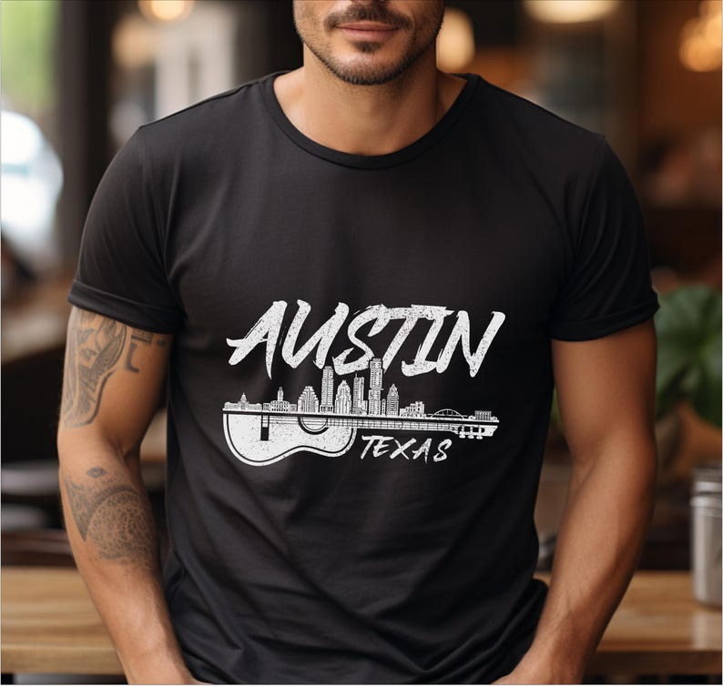 May include: Black t-shirt with a white graphic of the Austin, Texas skyline with the word "Austin" in a stylized font and the words "Texas" below the skyline. The skyline is depicted as a guitar with the buildings as the fretboard.