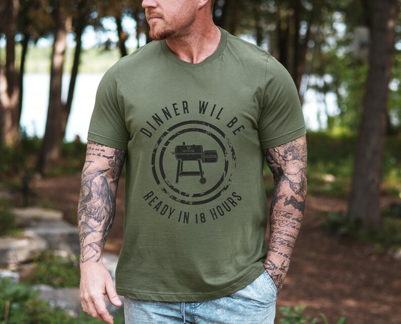 K&ouml;nnte beinhalten: Ein gr&uuml;nes T-Shirt mit einer schwarz-wei&szlig;en Grafik eines Smokers. Der Text auf dem Shirt lautet "Dinner will be ready in 18 hours".