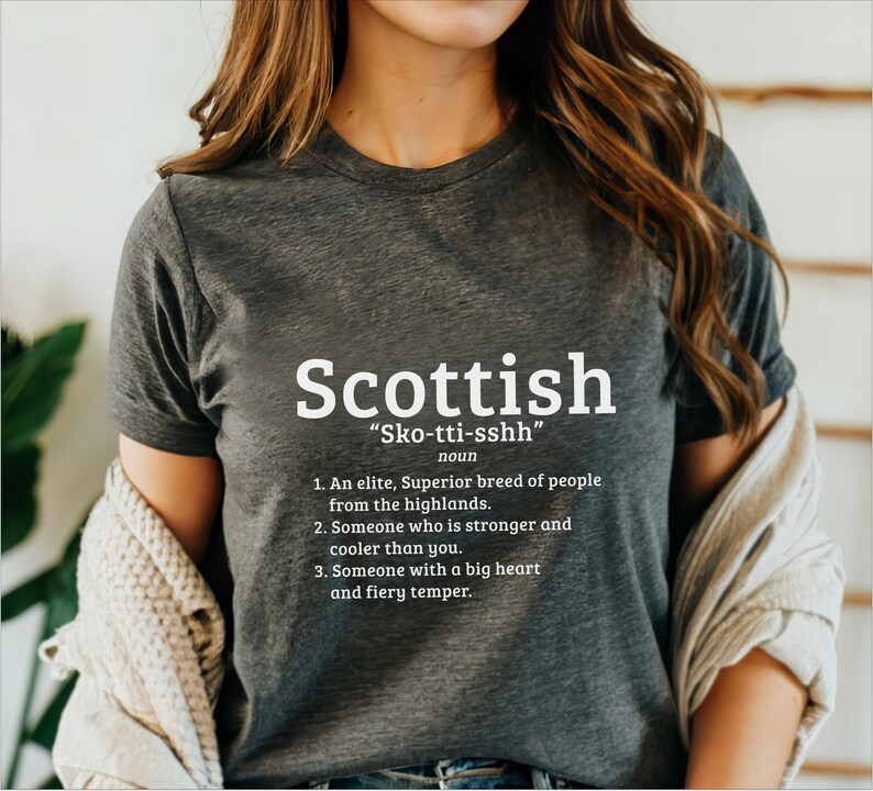 May include: A dark gray t-shirt with white text that reads "Scottish" and "Sko-tti-sshh" with a definition of the word. The definition includes the words "elite, superior breed of people, highlands, stronger, cooler, big heart, fiery temper."