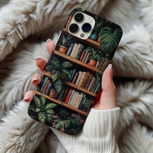 May include: A phone case with a design of a bookshelf filled with books and plants. The bookshelf is painted in a dark wood color with gold accents. The books are a variety of colors and sizes. The plants are green and leafy.