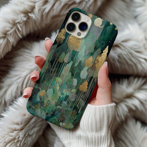 May include: A phone case featuring a forest design with gold and green trees. The case has a glossy finish and a dark green background. The design includes various shades of green and gold, creating a nature-inspired aesthetic.