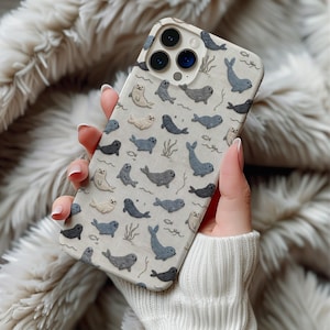 May include: A smartphone case with a light beige background featuring a repeating pattern of small embroidered-style seals in shades of grey, charcoal, and cream, interspersed with tiny fish and seaweed illustrations across the entire surface.