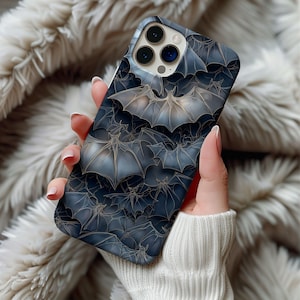 May include: A dark blue phone case featuring a repeating pattern of bats with gold-colored outlines. The bats have outstretched wings and are layered across the case. The case has a glossy finish and a camera cutout.