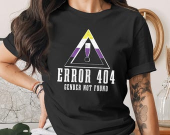 May include: Black t-shirt featuring a non-binary pride flag design within a warning triangle. The text "ERROR 404 GENDER NOT FOUND" is printed below the graphic in white, distressed font. The shirt has short sleeves.