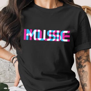 May include: Black t-shirt with the word "MUSSE" in a layered design of pink, blue, and white. The text is centered on the front of the shirt. The shirt has short sleeves.