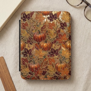 May include: A rectangular e-reader cover featuring a stained glass style pattern of orange pumpkins and multi-colored autumn leaves in shades of red, gold, and brown. The design includes dark outlines separating each leaf and pumpkin shape.