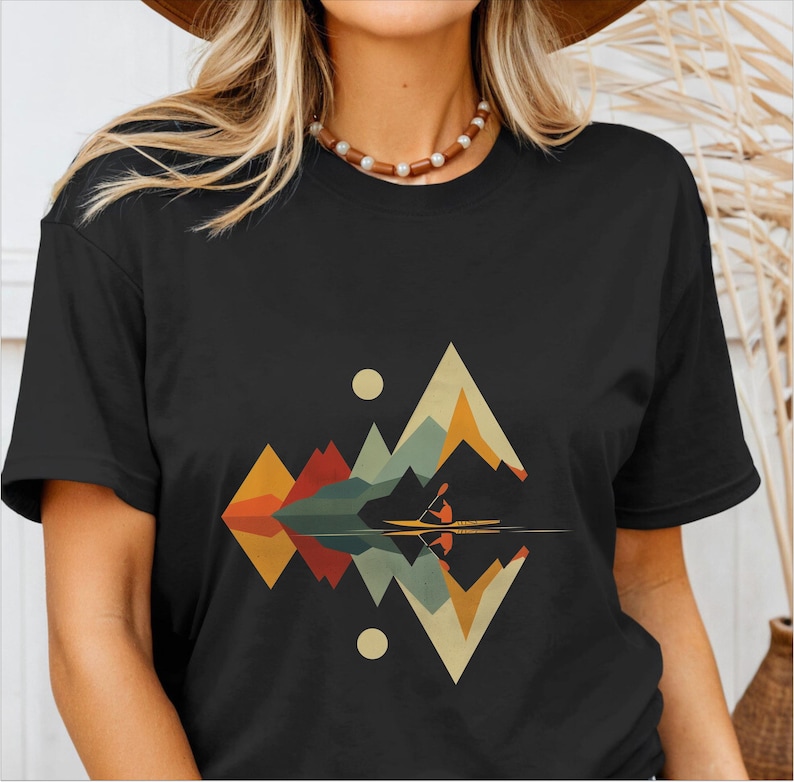 May include: A black t-shirt with a graphic design of a mountain range reflected in a lake with a person kayaking. The mountains are in shades of orange, yellow, green, and blue.
