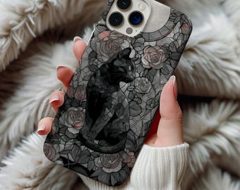 Könnte beinhalten: Eine Handyhülle mit einem schwarzen Katzendesign. Die Hülle hat ein grau-schwarzes Blumenmuster mit einem Glasmalerei-Effekt. Die Katze sitzt und schaut zur Seite. Die Hülle wird von einer Person gehalten, die einen weißen Pullover trägt.