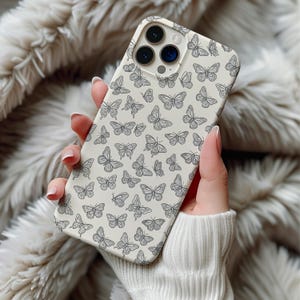 May include: A cream-colored phone case featuring a repeating pattern of black butterfly illustrations. The case has a smooth finish and is designed to fit a smartphone. The butterflies vary in size and are evenly spaced across the surface.