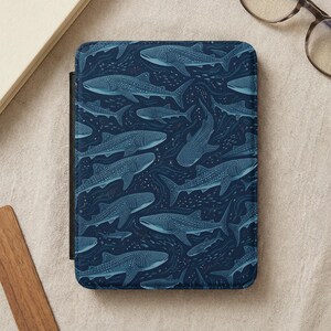 May include: A dark blue tablet case featuring a repeating pattern of whale sharks in varying sizes. The design includes small fish and wavy lines, creating an underwater scene. The case has a black border.