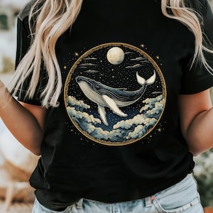 May include: Black t-shirt with a graphic of a whale jumping through the clouds with a full moon and stars in the background.