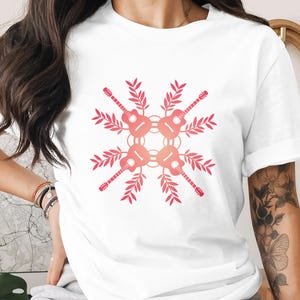 Peut inclure: T-shirt blanc avec un motif symétrique de guitares et de feuilles roses. Les guitares sont disposées en cercle, avec des feuilles qui s'étendent vers l'extérieur. Le motif est centré sur le t-shirt, créant une composition équilibrée.