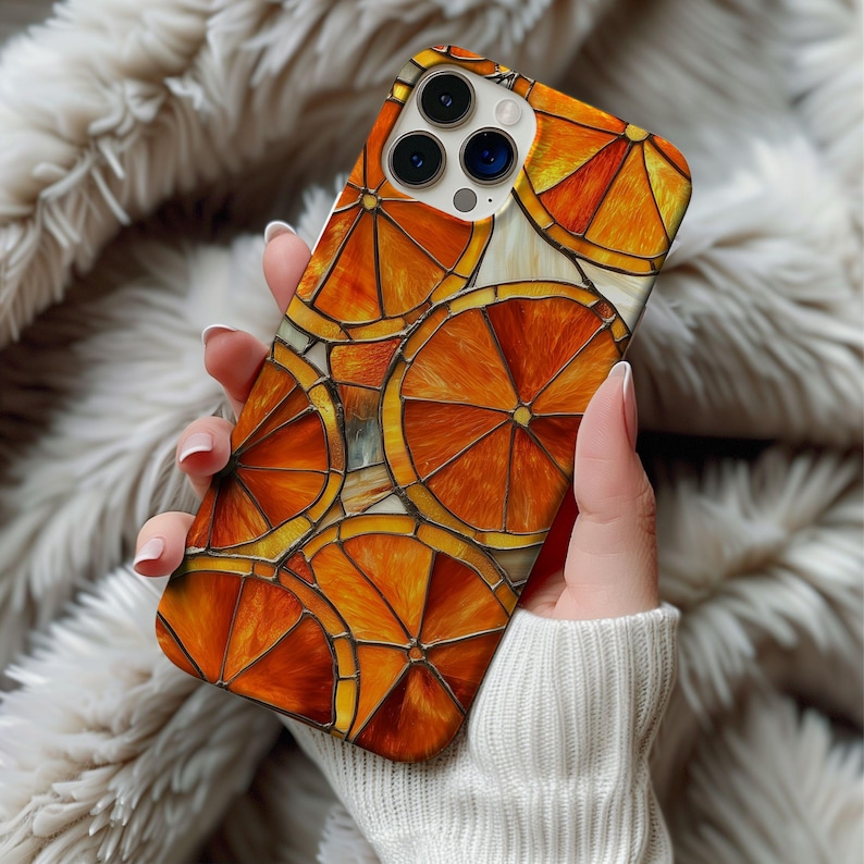 K&ouml;nnte beinhalten: Eine Handyh&uuml;lle mit einem lebendigen Design aus Orangenscheiben. Die H&uuml;lle hat eine gl&auml;nzende Oberfl&auml;che und ein sich wiederholendes Muster aus orangefarbenen und gelben Zitrusfr&uuml;chten. Die H&uuml;lle wird in der Hand einer Person gehalten, mit einem weichen, strukturierten Hintergrund.