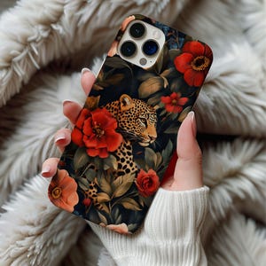 May include: A phone case featuring a leopard design surrounded by red flowers and green leaves against a dark background. The case has a glossy finish and a detailed illustration of the leopard's face and spots.