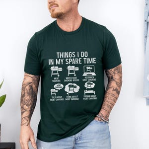 May include: Dark green t-shirt with the text "THINGS I DO IN MY SPARE TIME" and illustrations of meat smoking activities. The shirt features images of smokers, a laptop, and thought bubbles.
